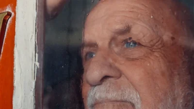 Primer plano de un hombre mayor con gesto serio mirando a través de una ventana
