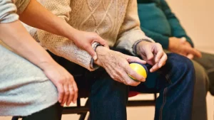 Manos de una cuidadora sosteniendo las manos de una persona mayor sentada