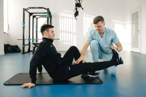 Fisioterapeuta trabajando con un paciente sentado en el suelo de un gimnasio de rehabilitación