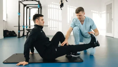 Fisioterapeuta trabajando con un paciente sentado en el suelo de un gimnasio de rehabilitación