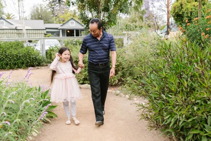 Abuelo paseando de la mano de su nieta por un jardín
