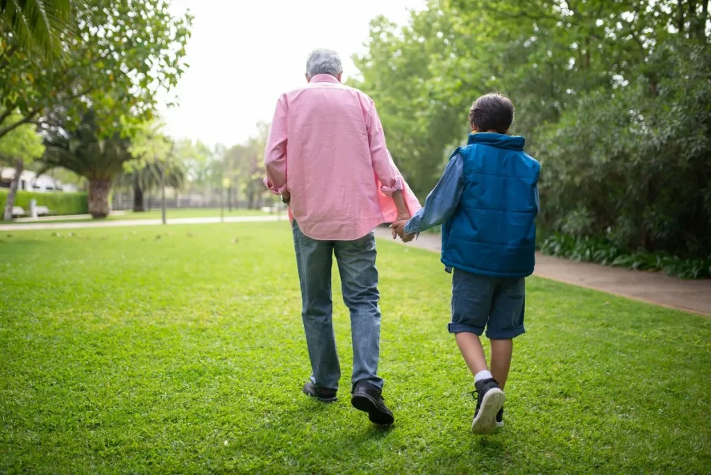 Hombre mayor caminando de la mano de un niño por un parque verde