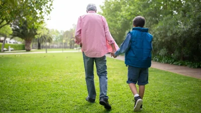 Hombre mayor caminando de la mano de un niño por un parque verde