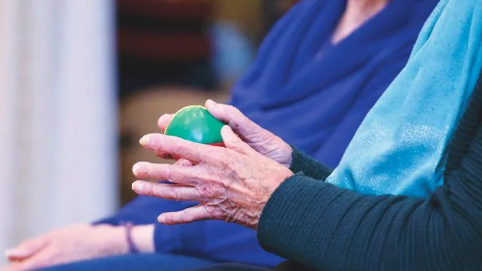Manos de una persona mayor apretando una pelota verde de terapia