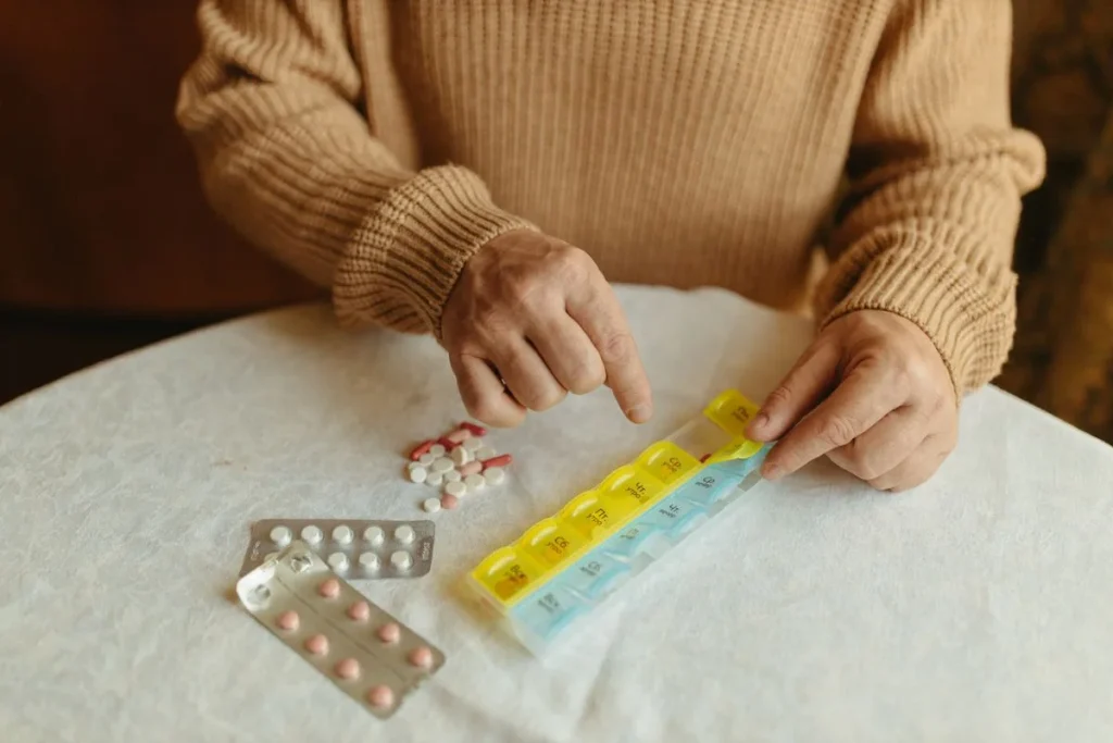 Manos de una persona mayor organizando pastillas en un pastillero semanal