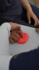 Mano trabajando una masilla terapéutica roja sobre una mesa