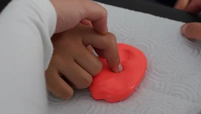 Mano trabajando una masilla terapéutica roja sobre una mesa
